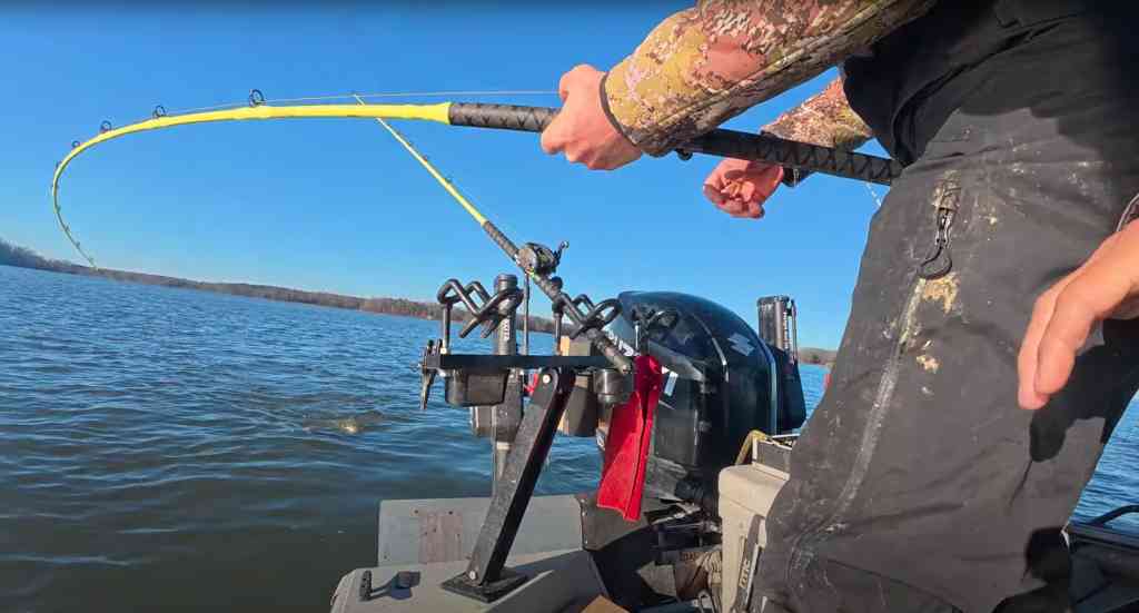 A bright-yellow rod bends deeply as an angler battles a catfish near the boat’s stern.