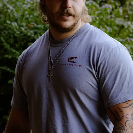 Catch The Fever® marketing director Dillon Weaver wearing a grey Catfish short sleeve lifestyle T‑shirt with a small red logo, standing outdoors.