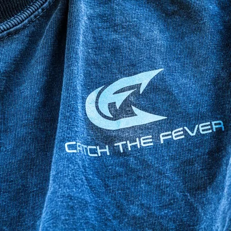 Close-up detail of the chest logo on a dark gray Catch The Fever® Crappie short sleeve lifestyle T shirt, showing the Catch The Fever® emblem and text.