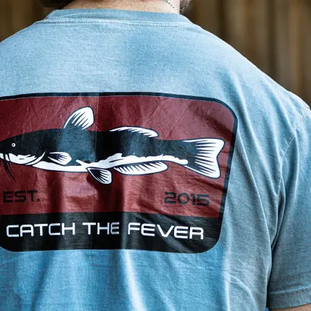 Back view of a grey Catfish short sleeve lifestyle T‑shirt worn by a model, featuring a large catfish graphic with the Catch The Fever® logo and 'EST. 2015' text.